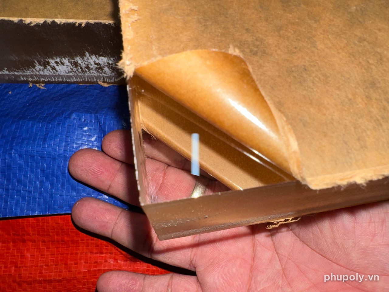Bóc giấy bảo vệ một góc miếng mica trong tại xưởng, nhìn xuyên thấy bàn tay