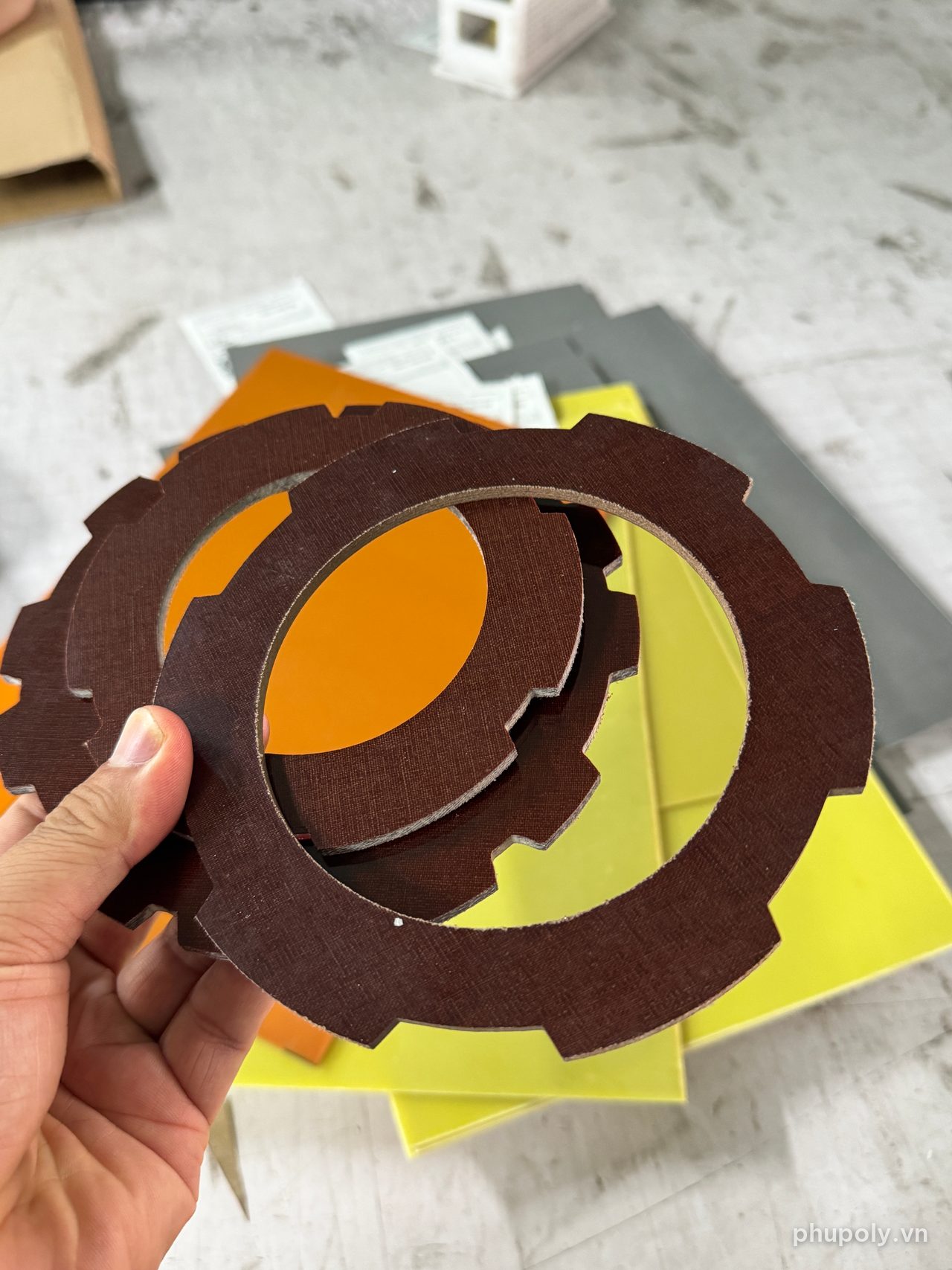 Hai chi tiết phíp vải bố màu nâu cắt CNC dạng bánh răng, cầm trên tay
