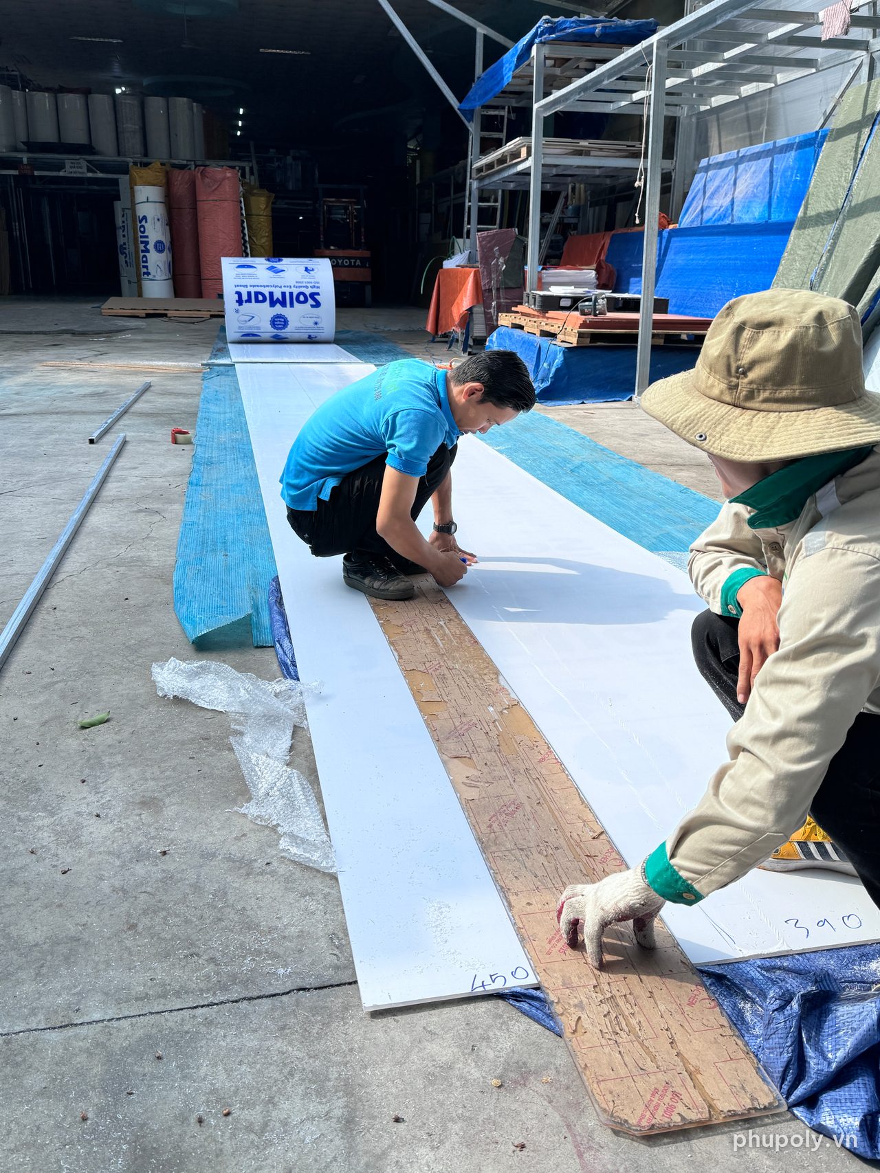 Hai thợ đo và đánh dấu đường cắt trên tấm poly đặc trắng sữa tại kho