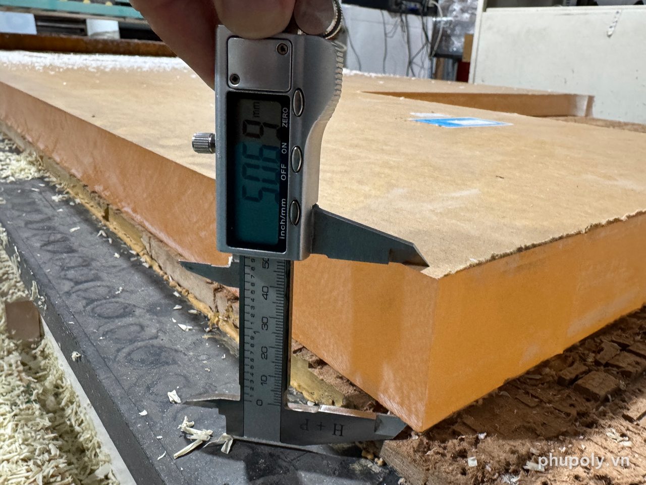 Thước kẹp điện tử đo tấm mica trong 50mm còn giấy bảo vệ trên bàn máy CNC, số đọc 50,69mm